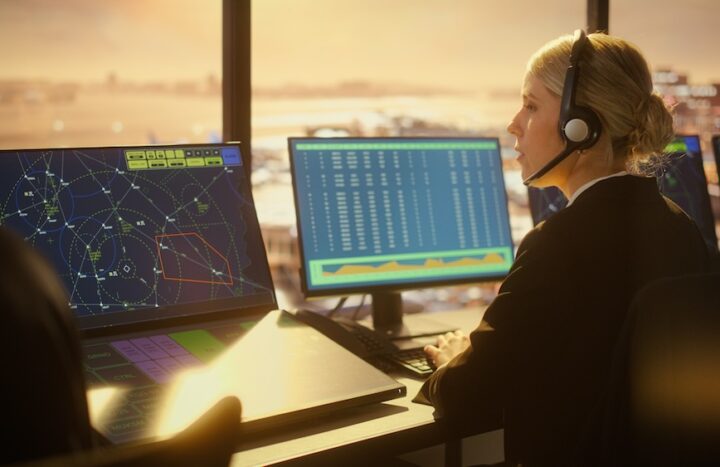 Female Air Traffic Controller with Headsets Talk in Airport Tower. Office Room Full of Desktop Computer Displays with Navigation Screens, Airplane Flight Radar Data for Controllers.
