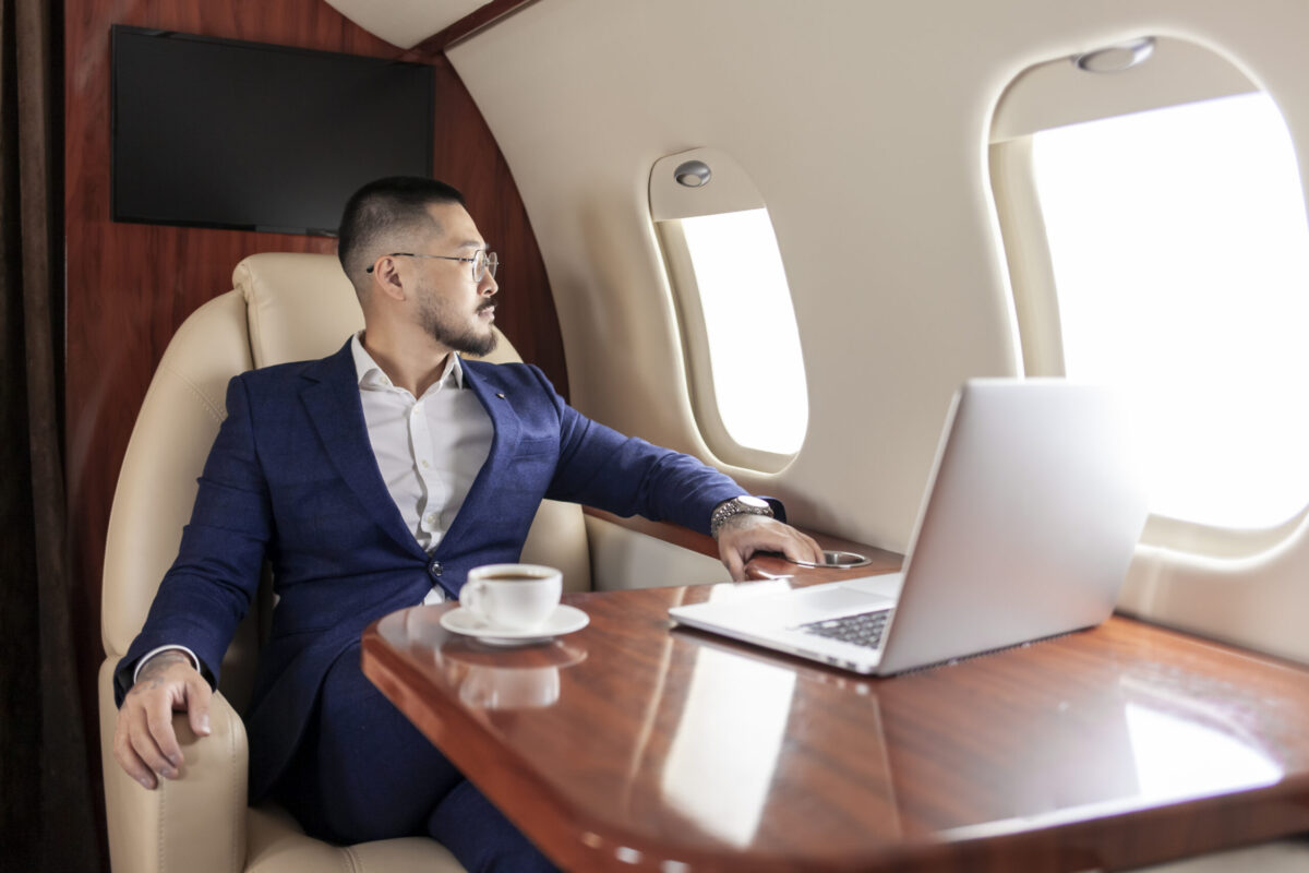 Business Jet Benefits | successful Asian businessman in suit and glasses flies in private luxury plane with laptop