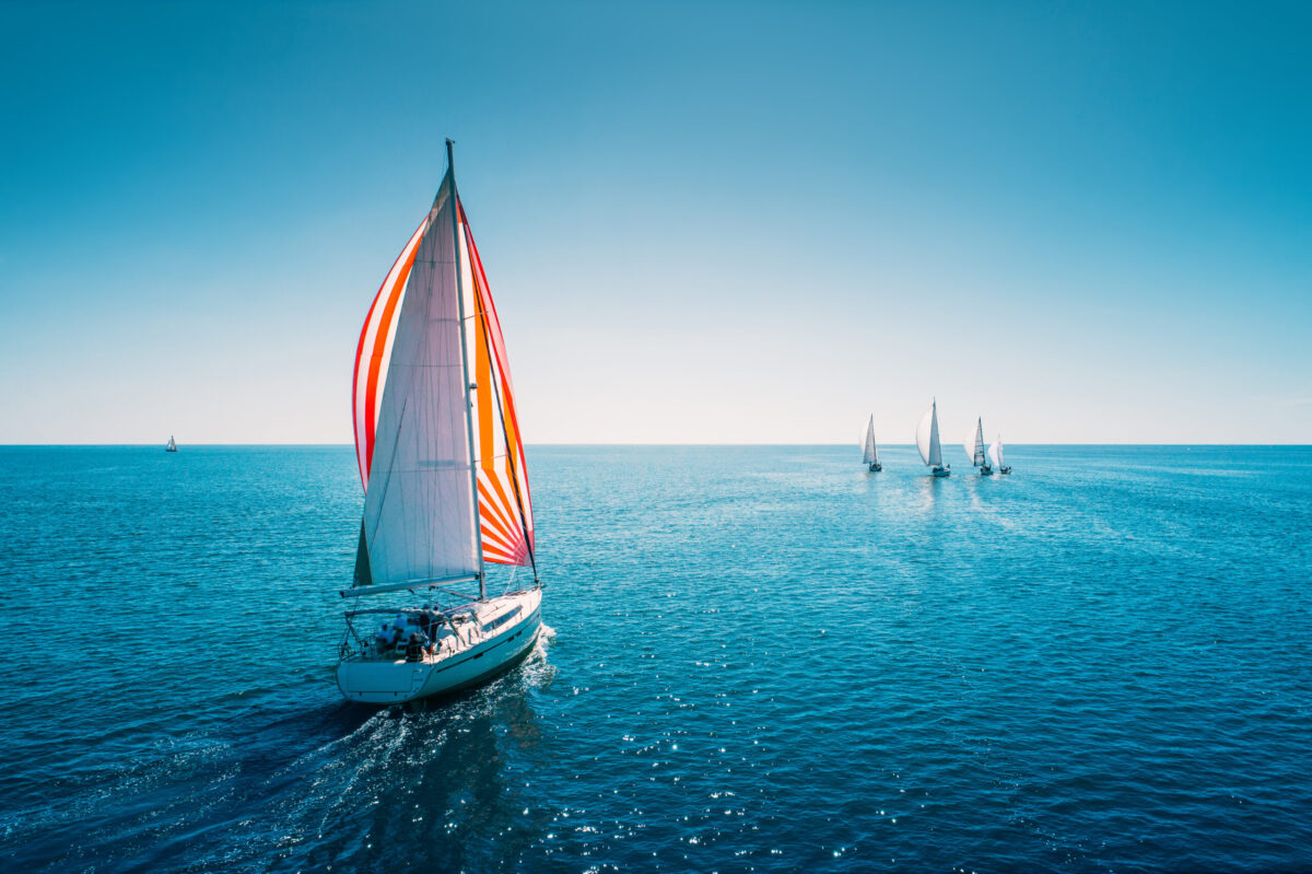 Regatta sailing ship yachts with white sails at opened sea. Aerial view of sailboat in windy condition. America's Cup 2024