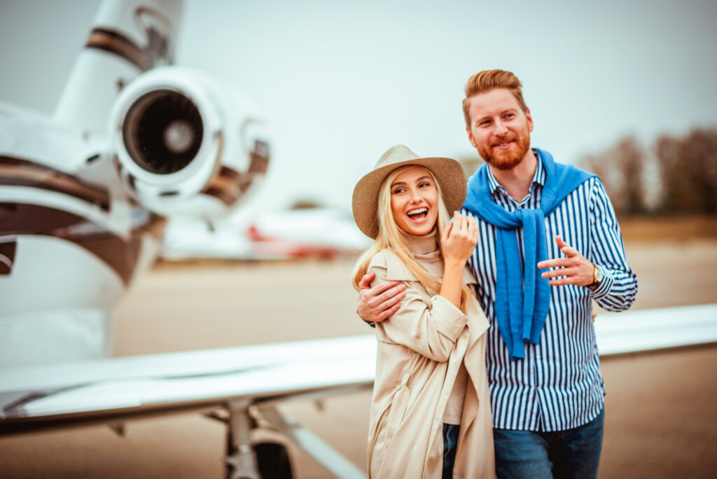 Young successful couple holding each other tight upon meeting each other next to a private airplane used for empty leg flights