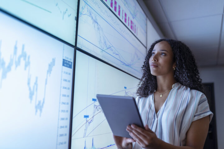 Businesswoman with tablet looking at charts on interactive screens for aircraft acquisition